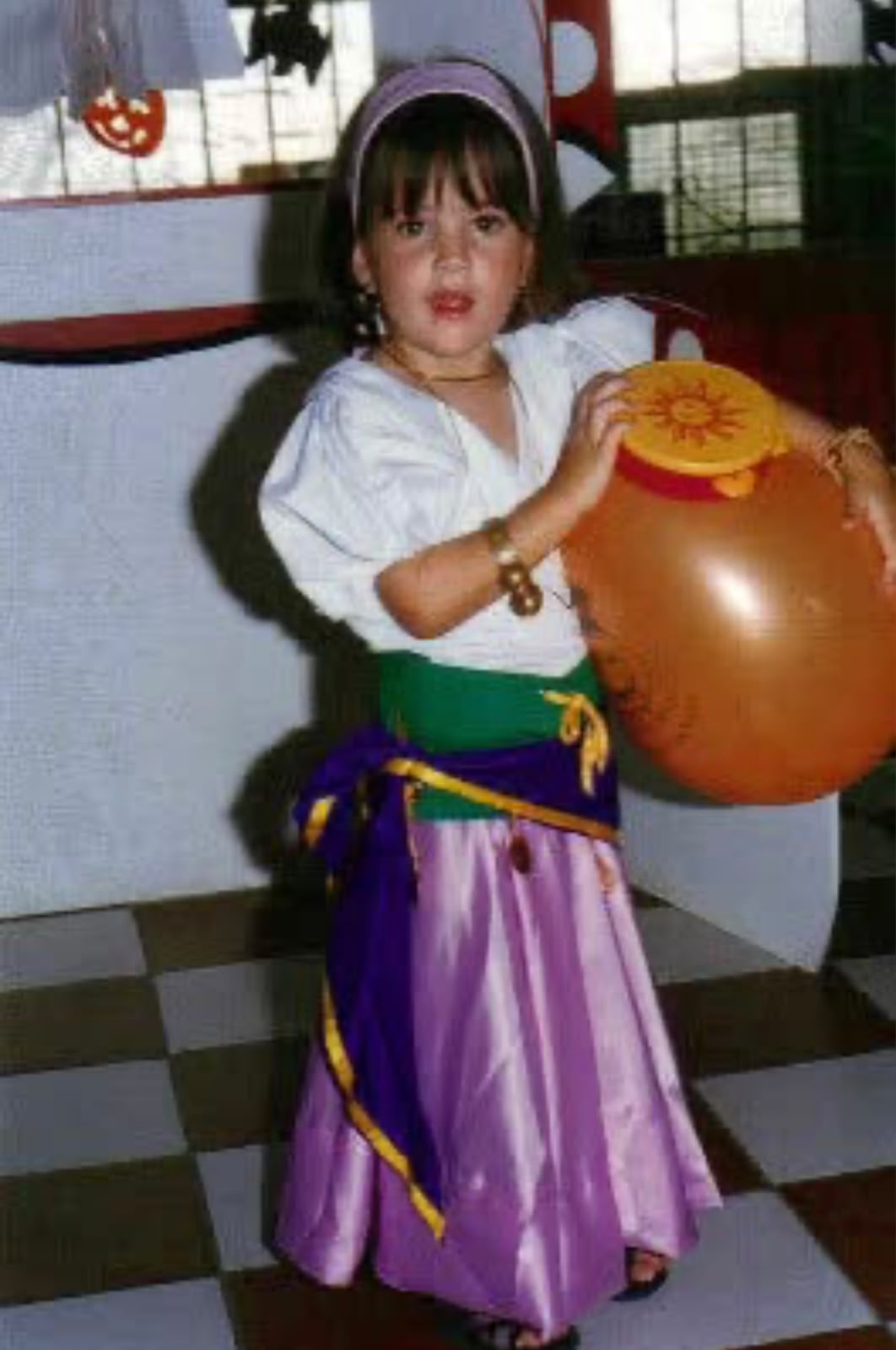 Niña disfrazada con falda lila y blusa blanca sosteniendo una vasija